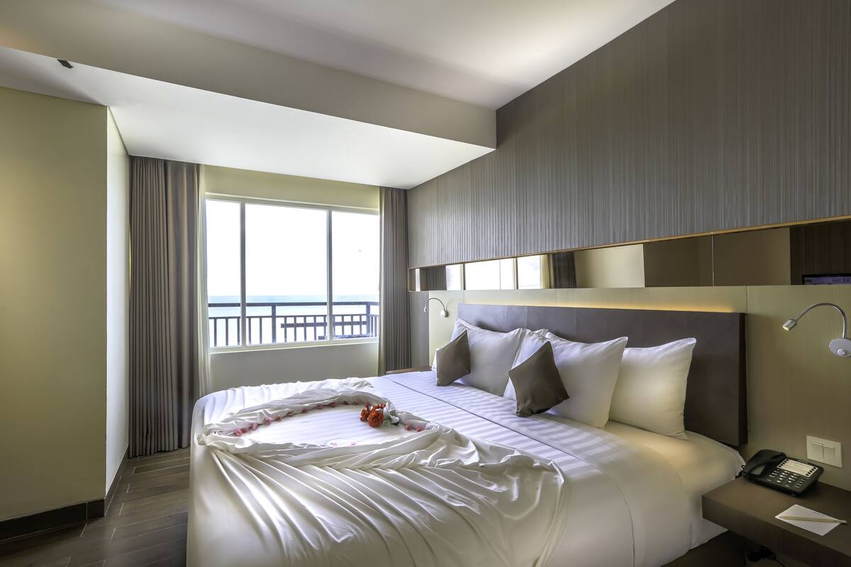 Une chambre d’hôtel avec un grand lit, une table de chevet avec un téléphone et une fenêtre avec des rideaux.