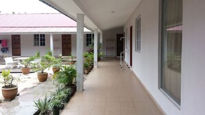 A covered corridor with potted plants, a white table, and chairs, leading to a building with a red roof. - Gelam Inn Motel Langkawi (Langkawi)