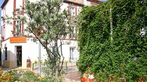 A building with a white facade, red trim, and a small garden area with flowers and a tree. - Hôtel Le Petit Château (Malakoff)