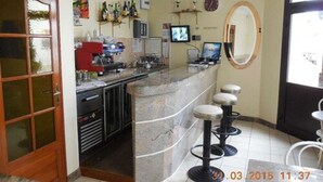A bar area with a counter, stools, a television, and various bottles on shelves. - Hôtel Le Petit Château (Malakoff)