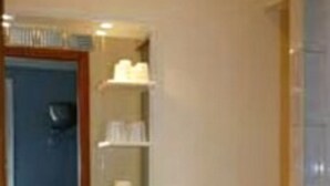 Un baño con lavamanos, espejo e inodoro. Hay repisas sobre el lavamanos y una toalla colgando en la pared.