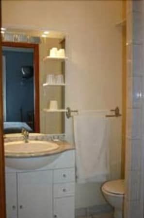 A bathroom with a sink, mirror, and toilet. There are shelves above the sink and a towel hanging on the wall. - Hôtel Le Petit Château (Malakoff)