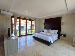 A bedroom with a large bed, a TV on a wooden desk, and a balcony with curtains.