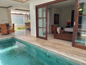 A swimming pool adjacent to a living area with a sofa and a dining table.