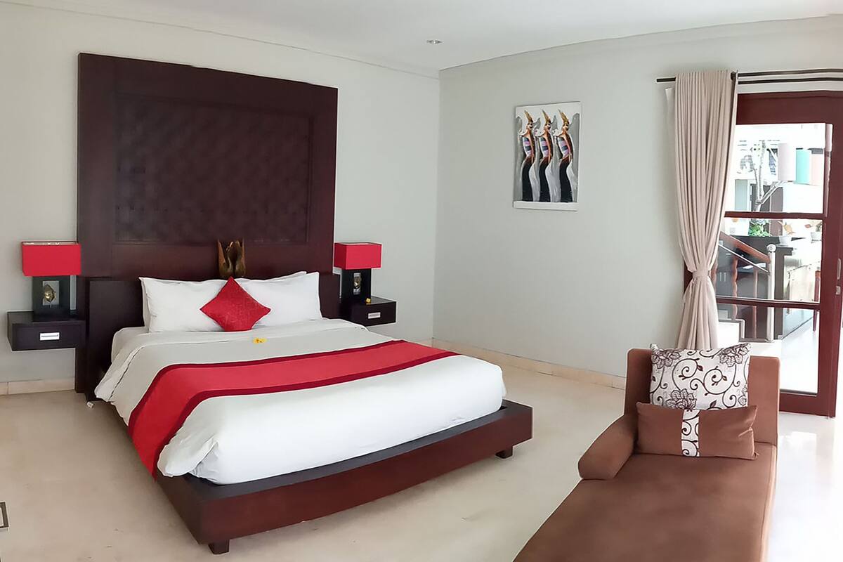 Quarto moderno com uma cama grande, duas mesas de cabeceira, um criado-mudo, um sofá e uma janela com cortinas.