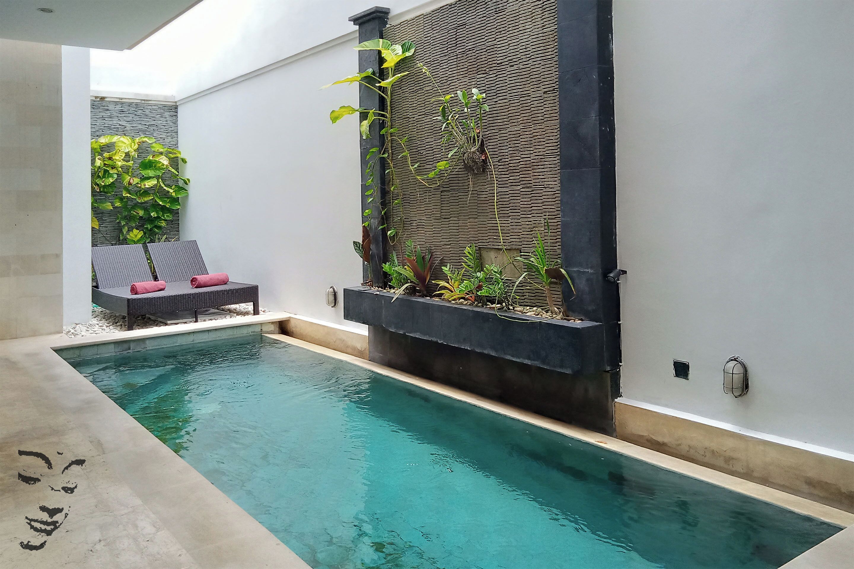 Una piscina dal design moderno, circondata da un muro bianco e un vaso nero con piante.