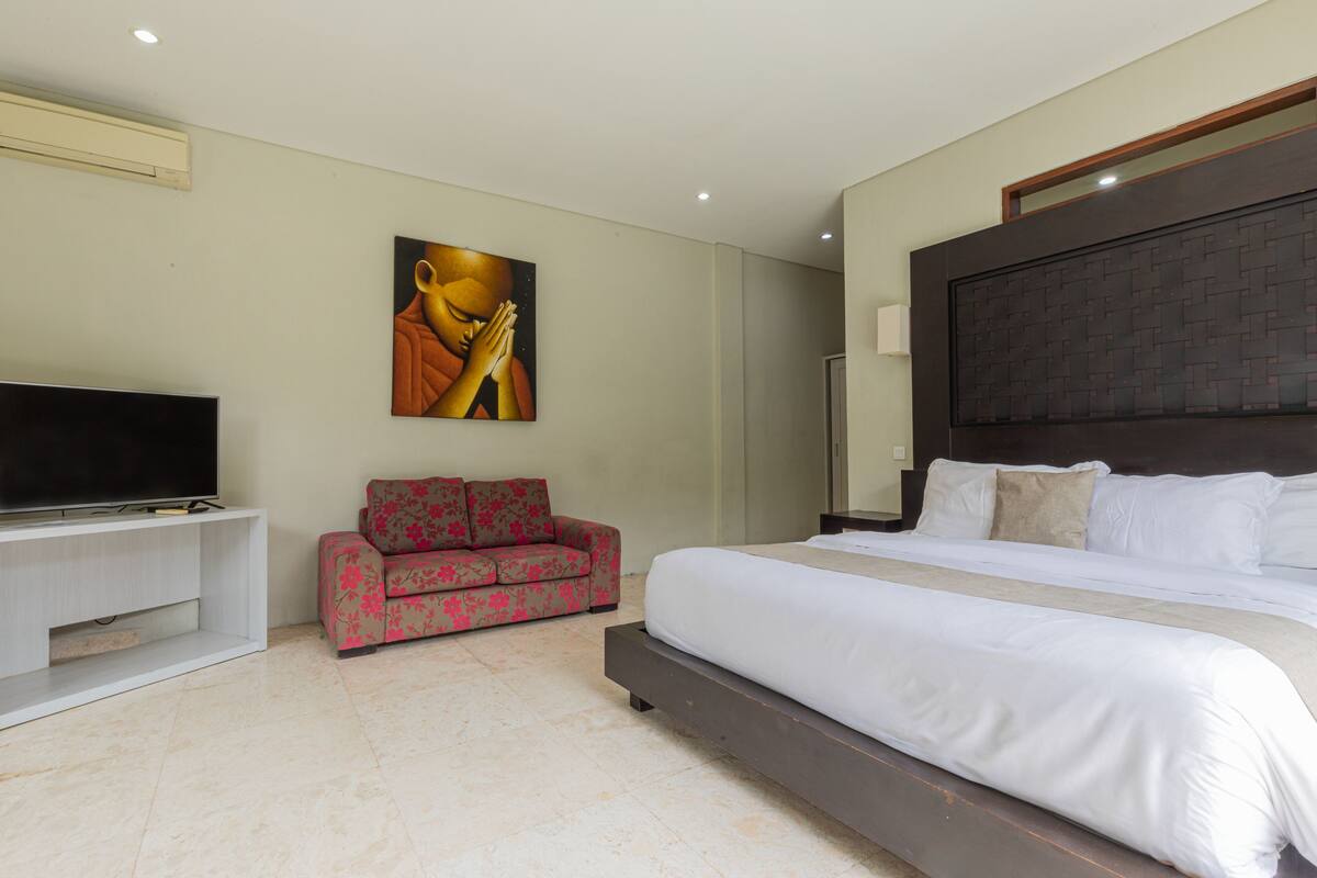 Quarto com cama grande, televisão de tela plana, sofá e pintura na parede.