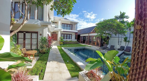 A modern house with a swimming pool, a well-maintained lawn, and a variety of plants.
