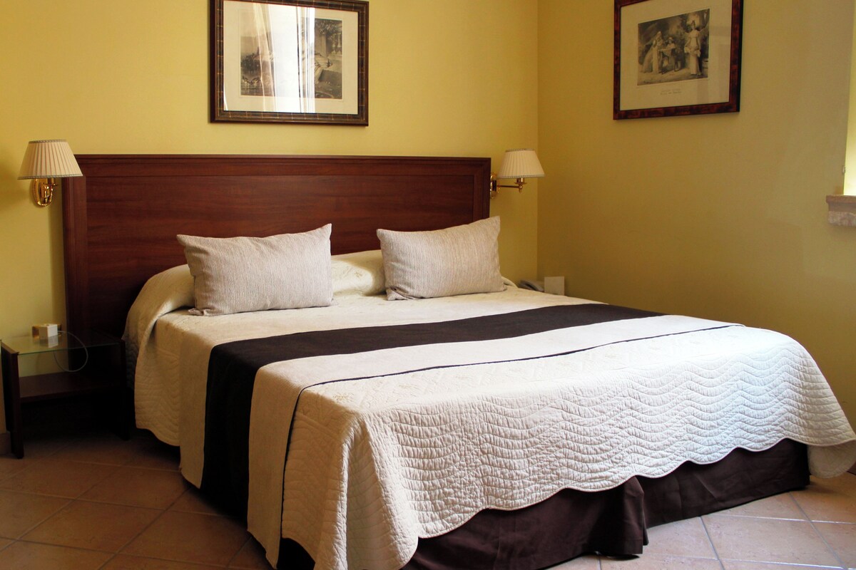 A double bed with a wooden headboard, two bedside lamps, and a quilted bedspread.