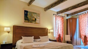 A neatly made bed with a wooden headboard, two bedside lamps, a nightstand, and a painting on the wall. - San Andrea Degli Armeni B&B di Charme - Dimora Storica (Taranto)