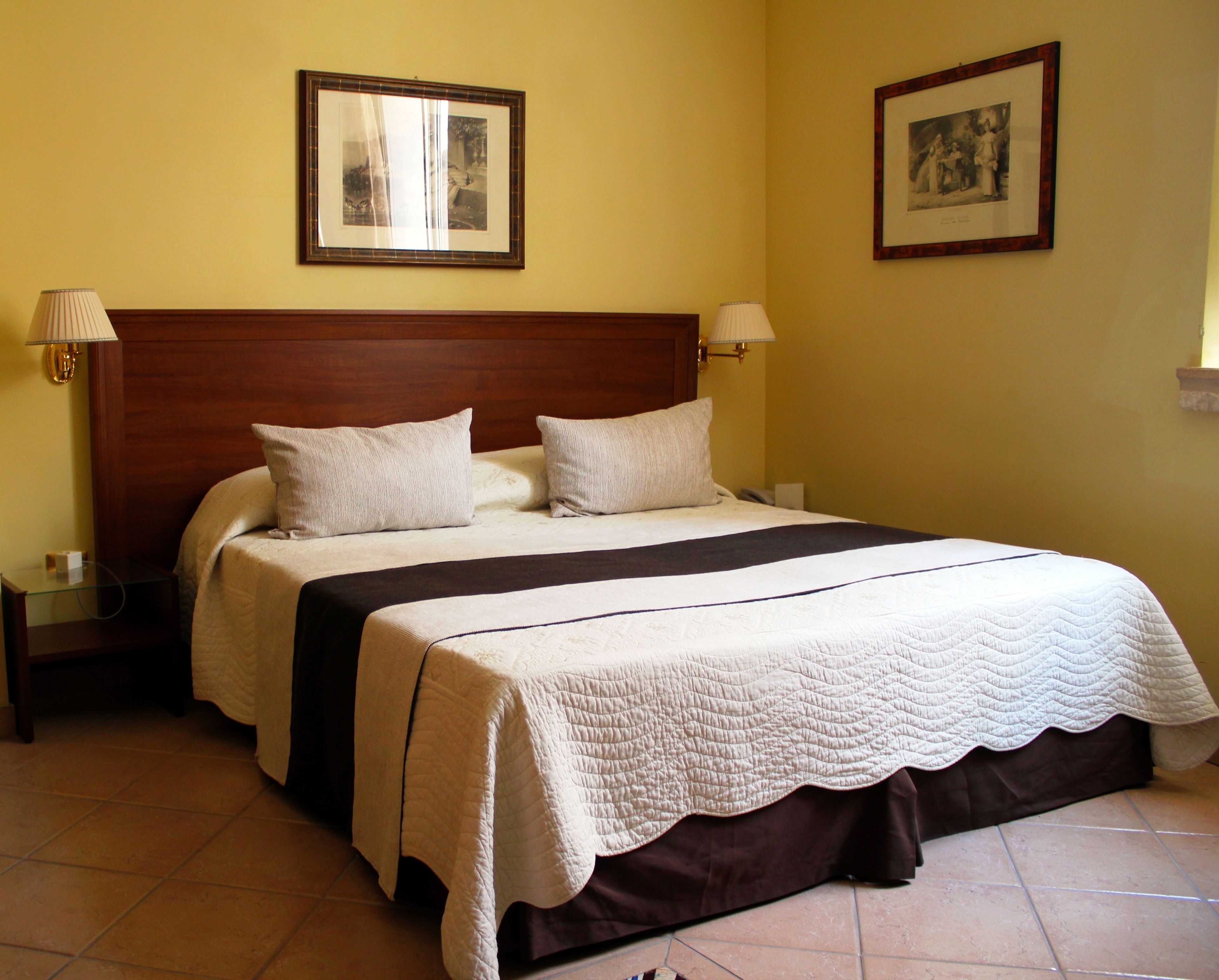 A double bed with a wooden headboard, two bedside lamps, and a quilted bedspread.