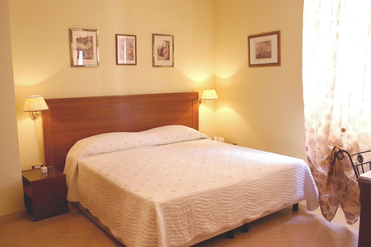 A neatly made bed with a wooden headboard, two bedside tables with lamps, and three framed pictures on the wall.