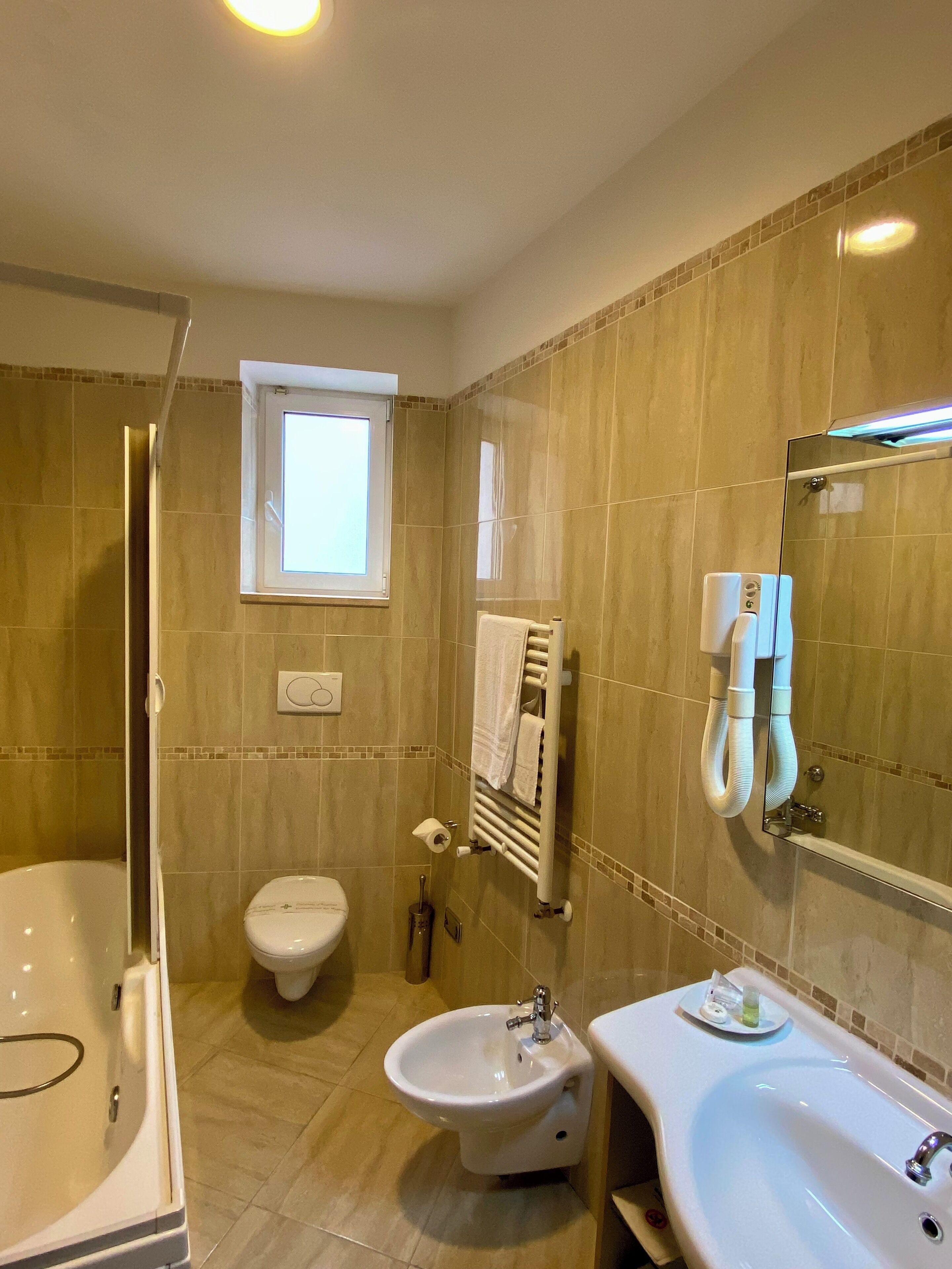 A bathroom with a bathtub, bidet, sink, and a window.