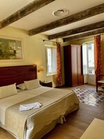 Una habitación de hotel con una cama grande, vigas de madera, un cuadro en la pared, una ventana con cortinas y un armario.