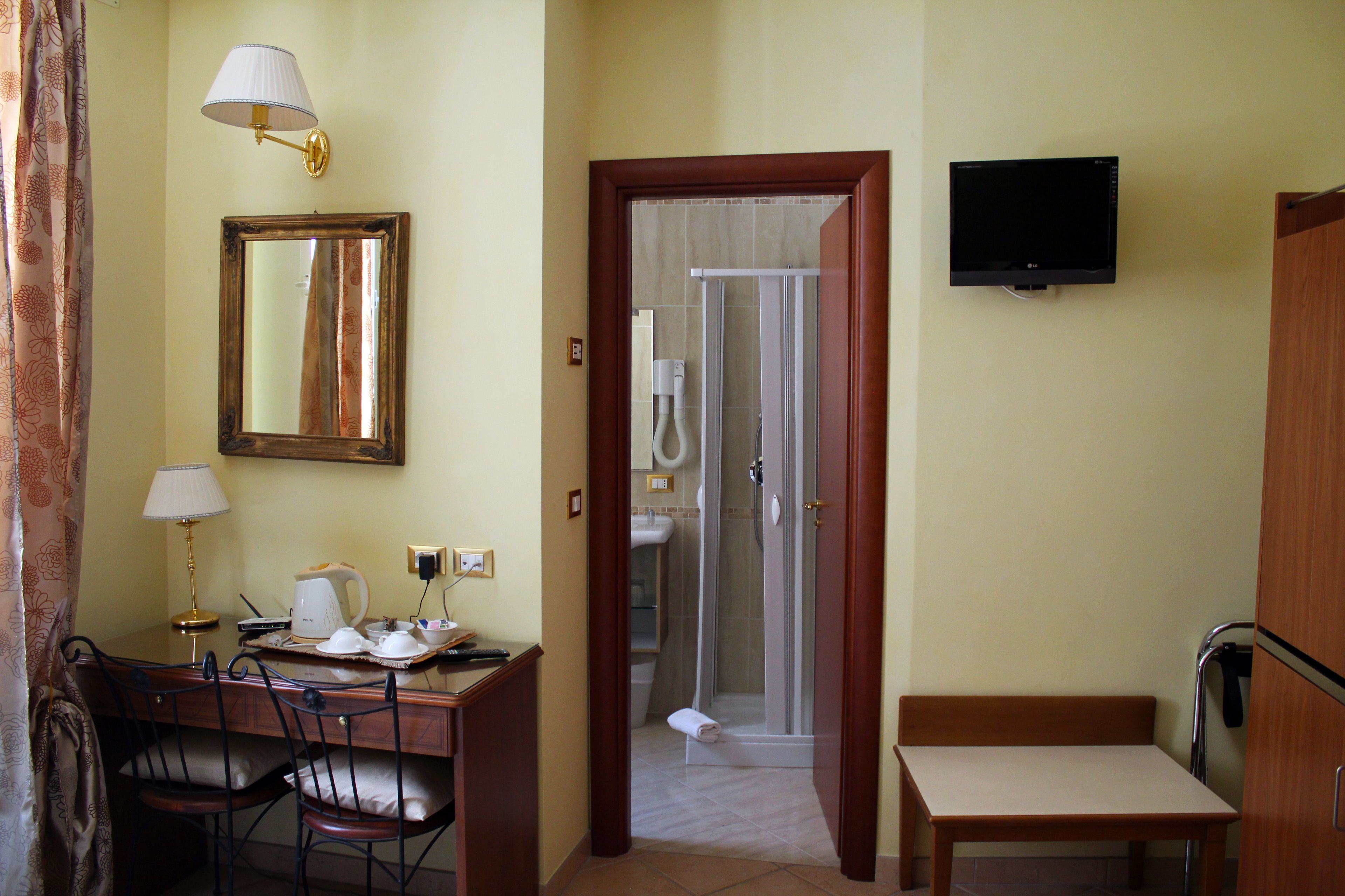 Una camera d'albergo con scrivania, sedie, televisore, cabina doccia e un letto.