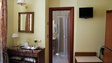 Una camera d'albergo con scrivania, sedie, televisore, cabina doccia e un letto.