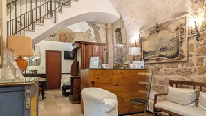 A spacious living area with a staircase, a wooden reception desk, a white sofa, and a painting on the wall. - San Andrea Degli Armeni B&B di Charme - Dimora Storica (Taranto)
