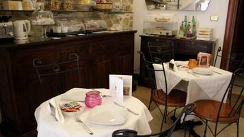 Un comedor con una mesa dispuesta para dos, una cafetera y una barra con distintos alimentos.