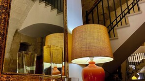 A room with a large ornate mirror, a staircase, and a table with candles and a lamp. - San Andrea Degli Armeni B&B di Charme - Dimora Storica (Taranto)