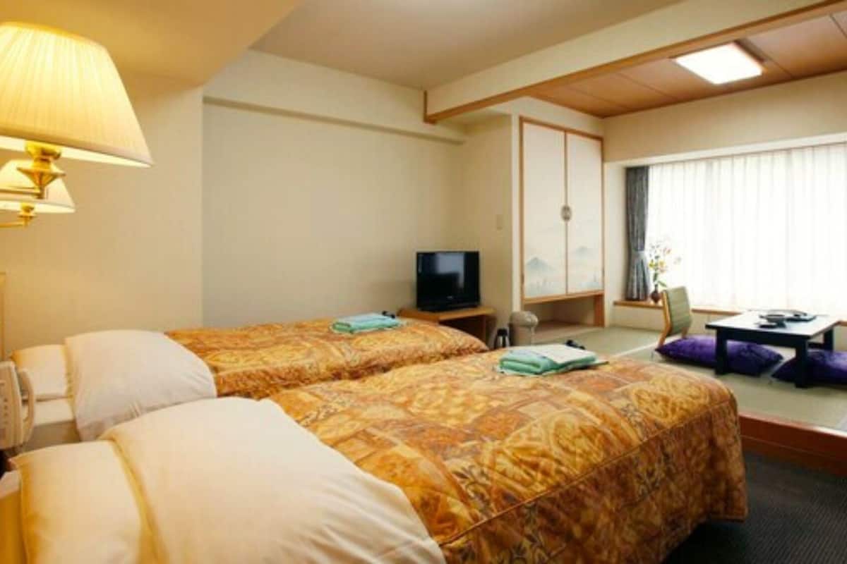 Une chambre d’hôtel avec deux lits, une télévision, un bureau et une fenêtre avec des stores.