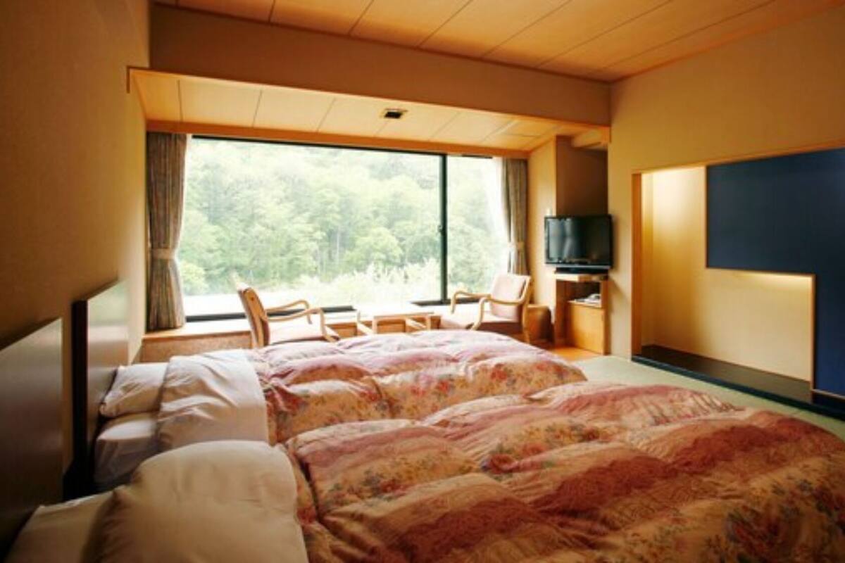 Une chambre d’hôtel avec deux lits, une télévision, une chaise et une grande fenêtre donnant sur des arbres.