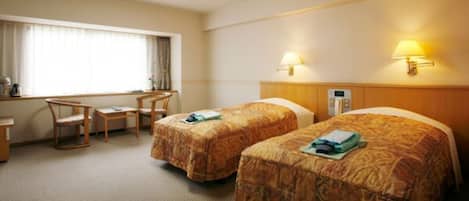 Habitación de hotel con dos camas, un escritorio y una silla. Cuenta con una ventana con cortinas, una lámpara de pared y un termostato.