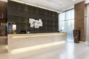 A hotel reception desk with a modern design, featuring a dark patterned wall and a marble counter.