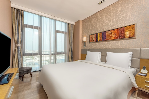 Une chambre d’hôtel avec un grand lit, une télévision, un bureau et une fenêtre avec des rideaux.