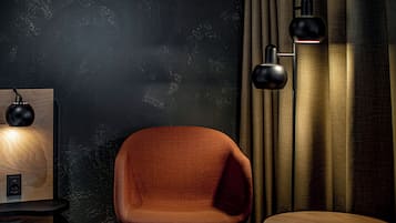 A room with a dark textured wall, a wooden side table with a lamp, a modern chair, and a floor lamp.