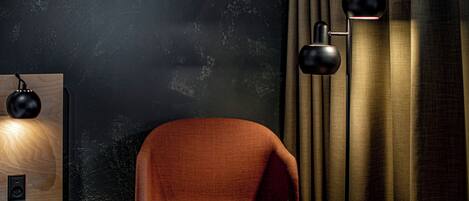 Een kamer met een donkere, structuurrijke muur, een houten bijzettafeltje met een lamp, een moderne stoel en een vloerlamp.