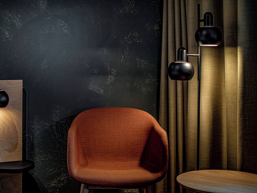 A room with a dark textured wall, a wooden side table with a lamp, a modern chair, and a floor lamp.