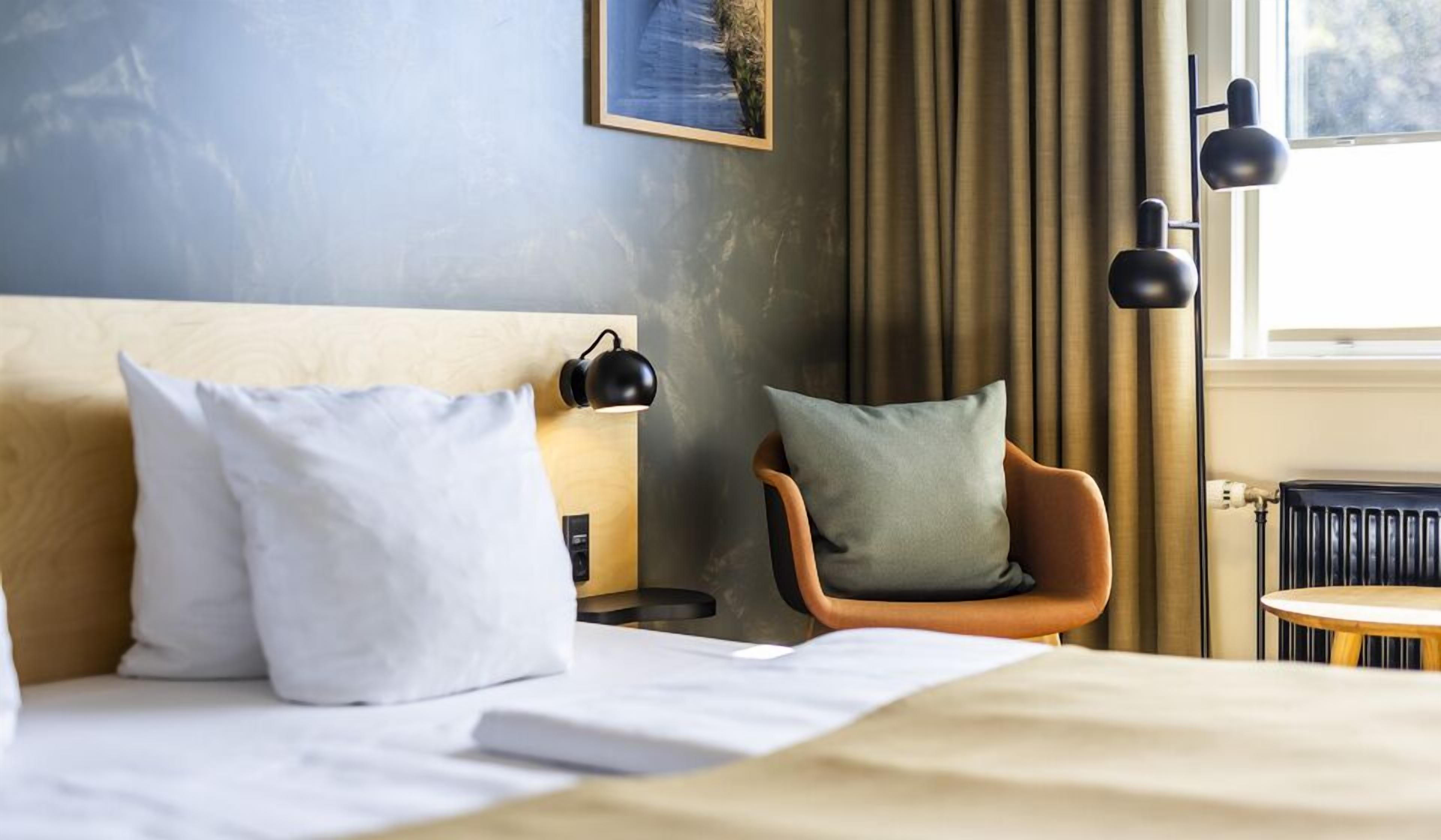 Habitación de hotel con cama, una silla, mesita de noche y ventana con cortinas.