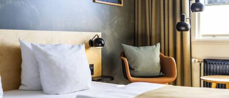 Habitación de hotel con cama, una silla, mesita de noche y ventana con cortinas.