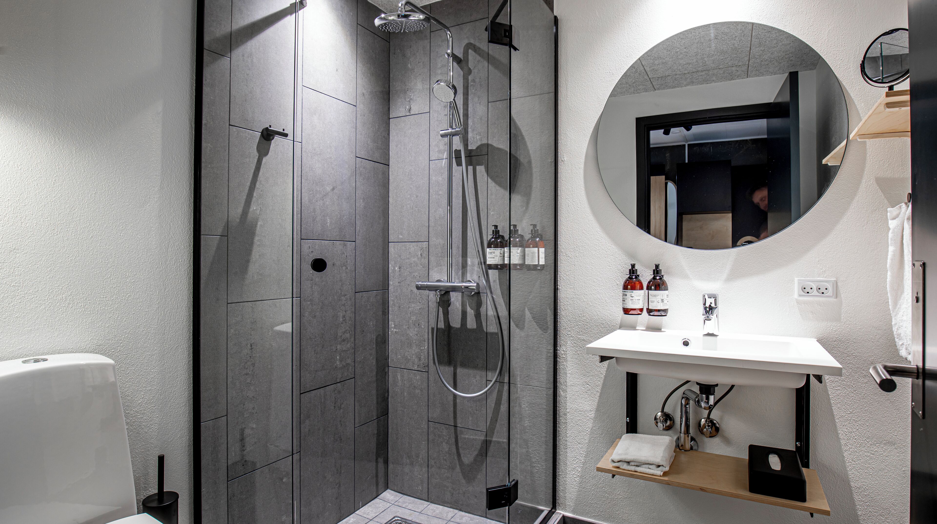 Un baño moderno con cabina de ducha, un espejo redondo y un lavabo blanco.