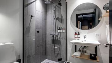 Un baño moderno con cabina de ducha, un espejo redondo y un lavabo blanco.
