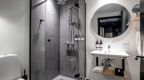 A modern bathroom with a walk-in shower, a round mirror, and a white sink.