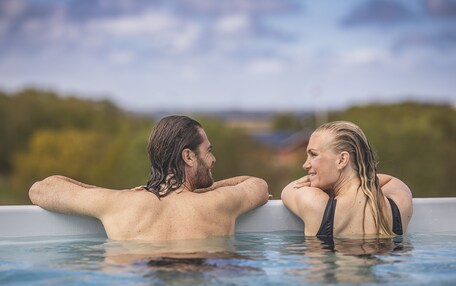 Two people in a hot tub with a natural landscape in the background.