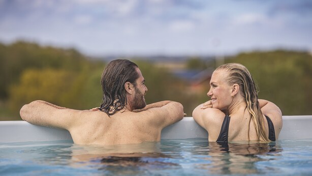 Two people in a hot tub with a natural landscape in the background. - Fjordgaarden - Spa - Hotel - Konference (Ringkobing)