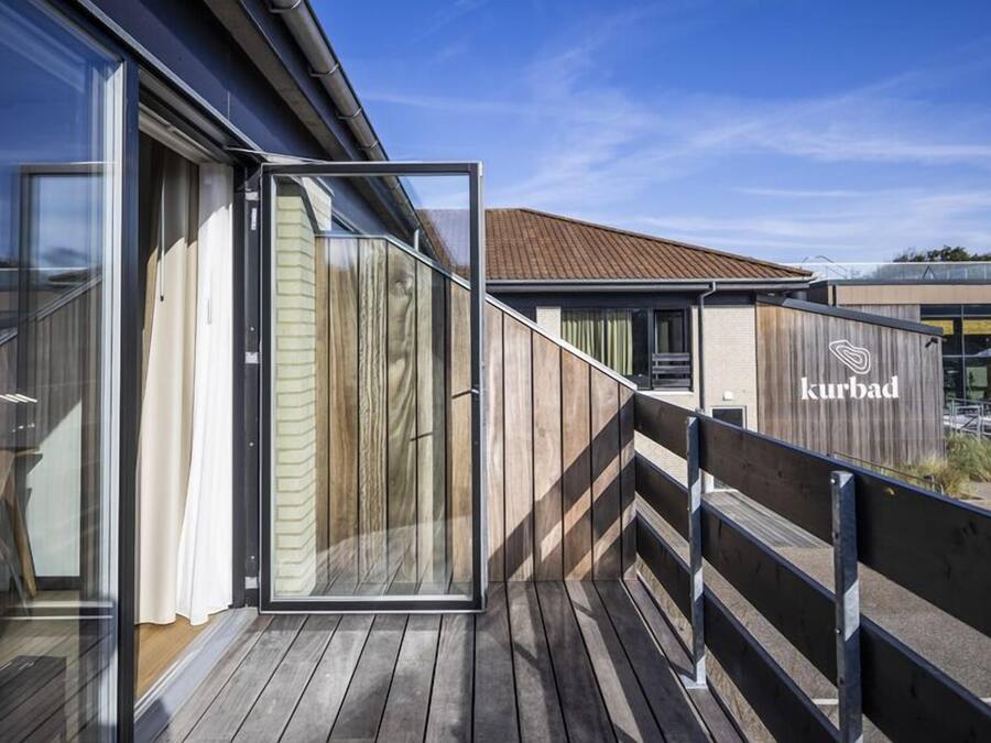 Een modern gebouw met een houten terras, glazen deuren en een bordje met de tekst 'kurbad'.