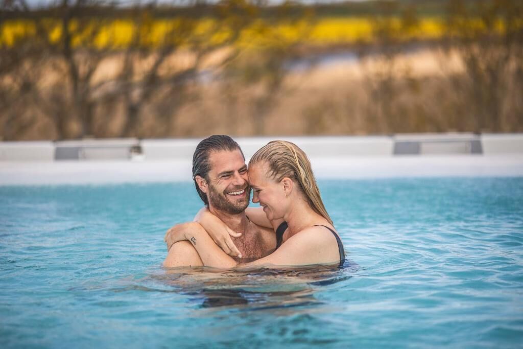 Una pareja abrazándose en una piscina cristalina con un fondo natural desenfocado.