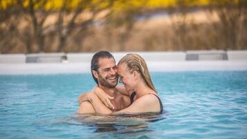 Una pareja abrazándose en una piscina cristalina con un fondo natural desenfocado.