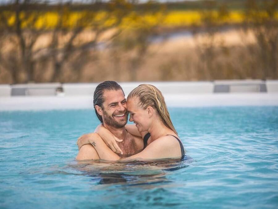 Una pareja abrazándose en una piscina cristalina con un fondo natural desenfocado.