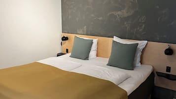 Un lit bien fait, recouvert d’une couverture marron, avec deux oreillers et une tête de lit adossée à un mur à texture.