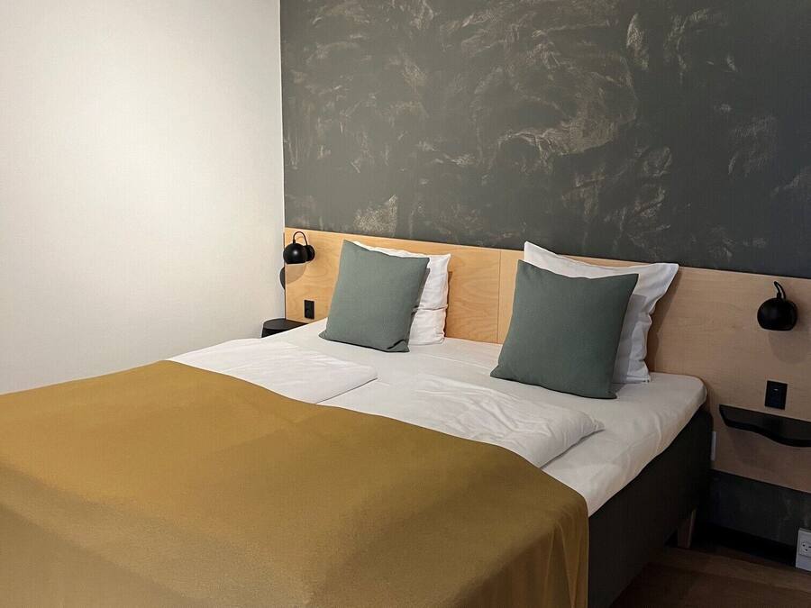 A neatly made bed with a brown bedspread, two pillows, and a headboard against a textured wall.