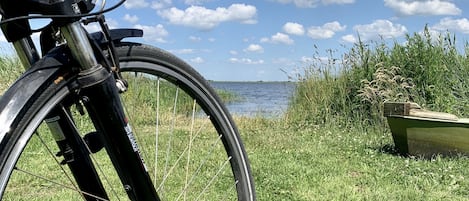 A bicycle parked on grass with a lake and clouds in the background.