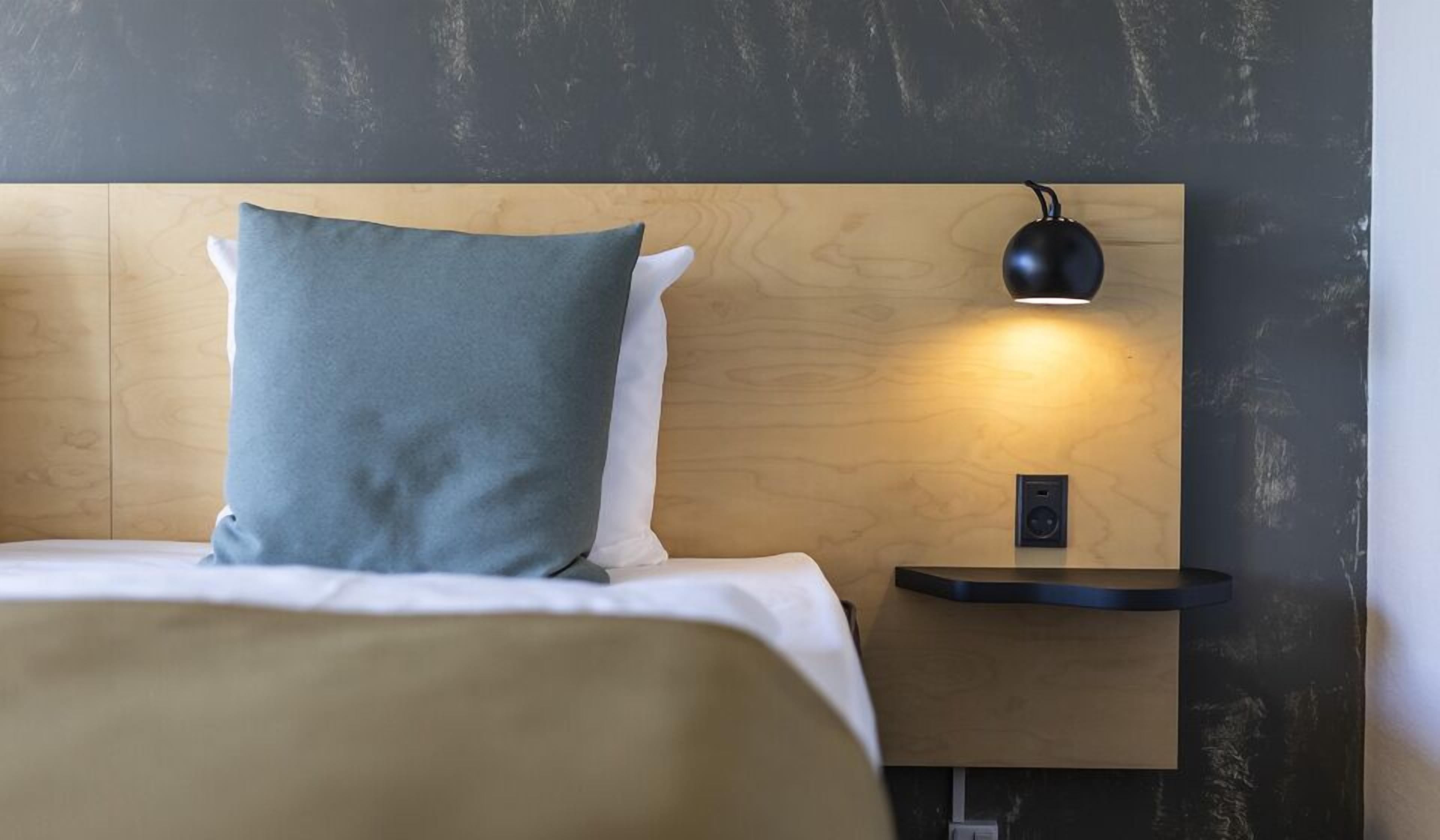 A neatly made bed with a blue and white pillow, a wooden headboard, and a bedside table with a black lamp.