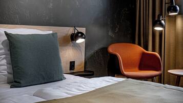 A modern hotel room with a wooden headboard, a green pillow, a wooden chair, and two black floor lamps.