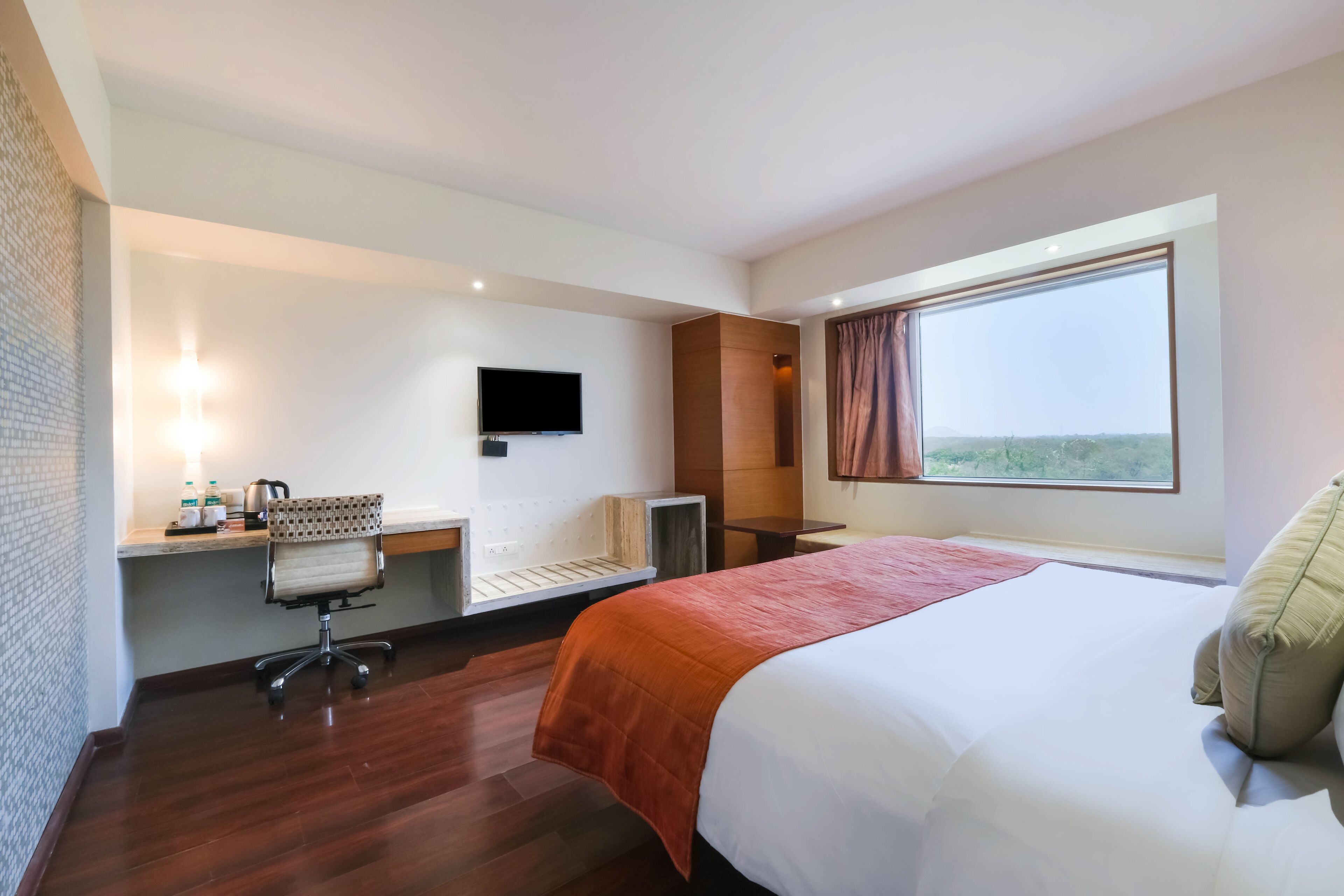 Habitación de hotel con una cama grande, un escritorio con silla, un televisor y una ventana con vistas.