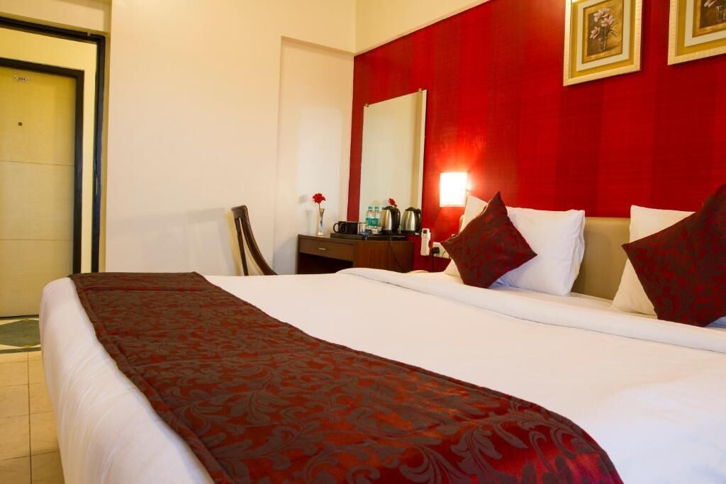 A hotel room with a large bed, a desk with a chair, a mirror, and a red accent wall.