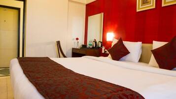 A hotel room with a large bed, a desk with a chair, a mirror, and a red accent wall.